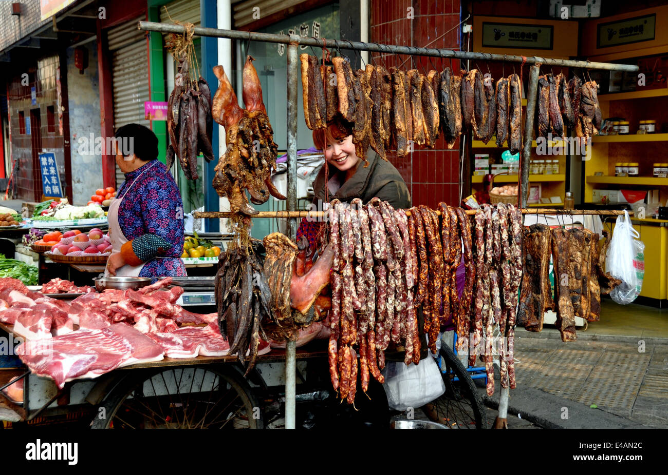 PENGZHOU, CINA: donne a un macellaio outdoor negozio di vendita di tagli di carne di maiale viene visualizzata su un tavolo e carni secche e salsicce display Foto Stock