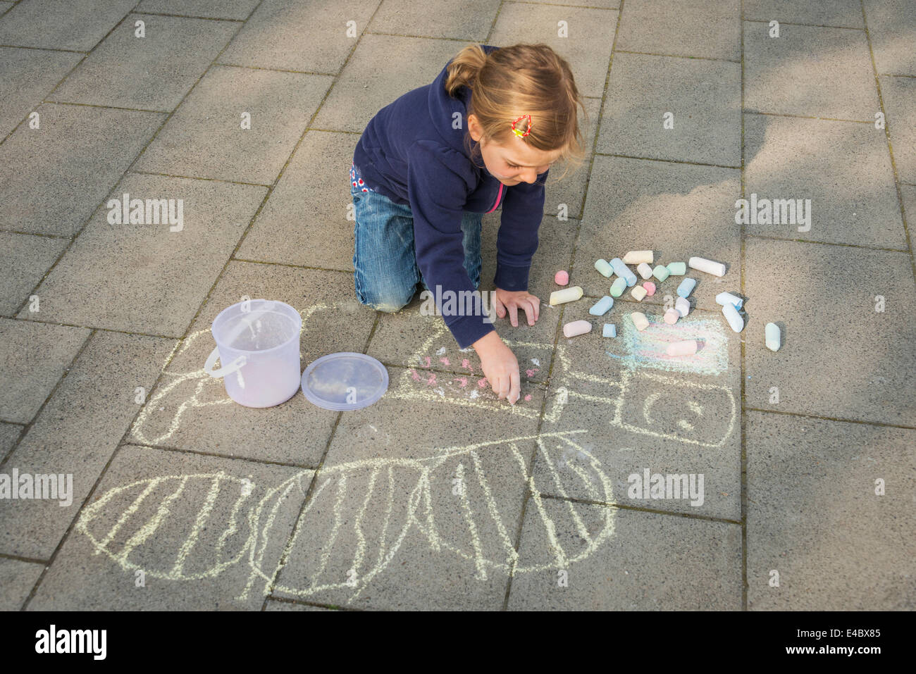 Ragazza bionda disegno con un gessetto sul marciapiede, Monaco di Baviera, Germania Foto Stock