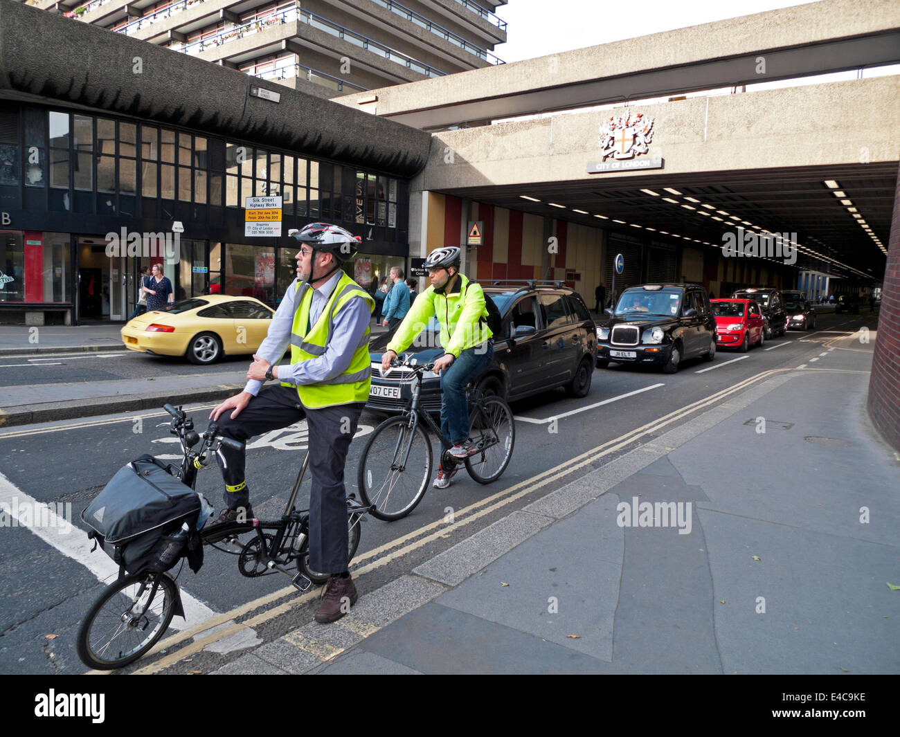 Uomini d'affari impiegati pendolari indossando caschi ciclismo casa dopo il lavoro in attesa di biciclette per il semaforo Barbican London UK KATHY DEWITT Foto Stock