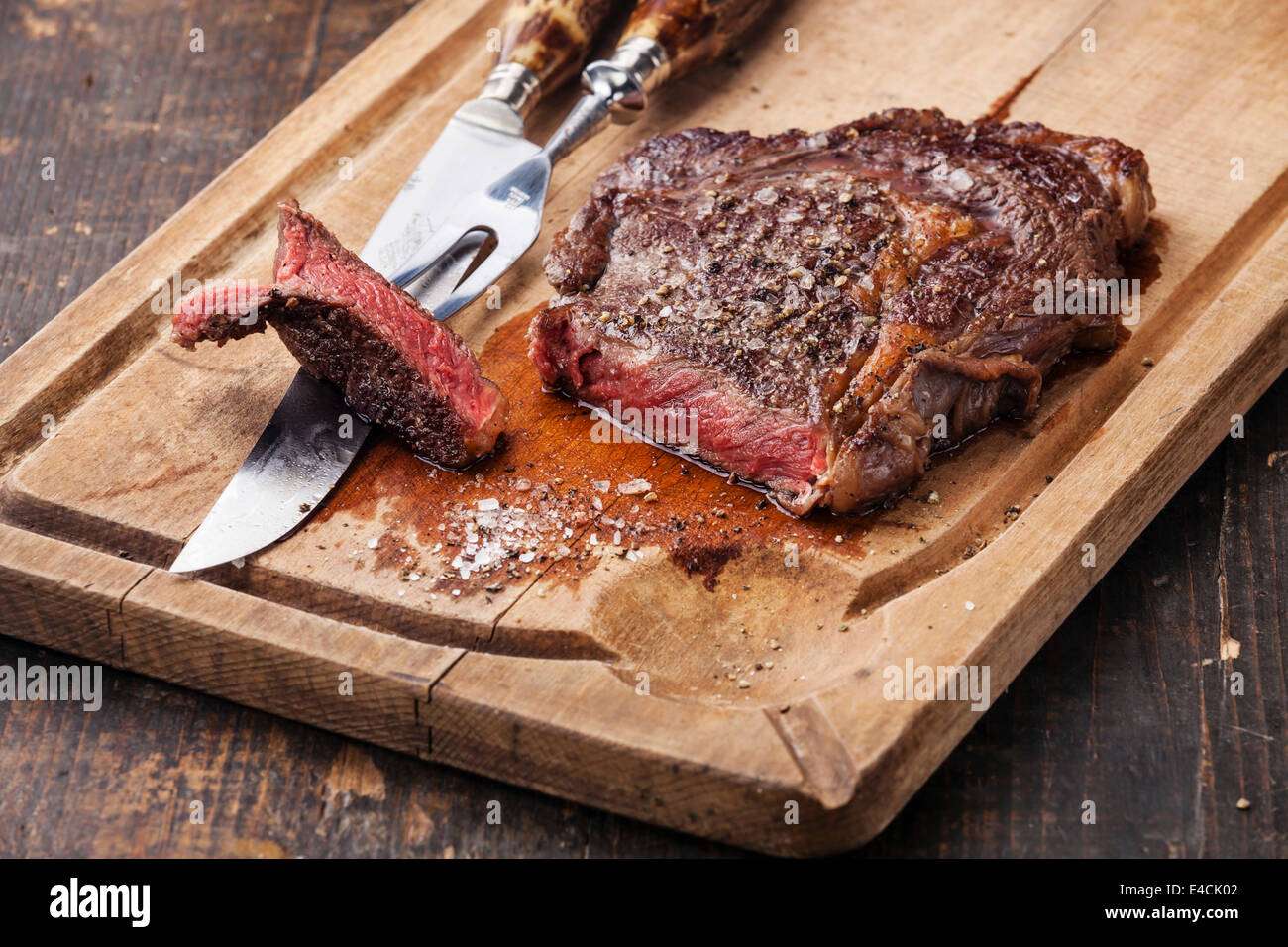 Mezzo raro grigliate di carne di manzo bistecca con coltello e forchetta per la carne sul tagliere in legno scuro dello sfondo Foto Stock