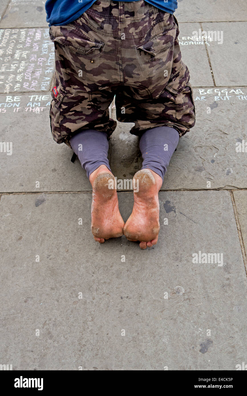 Un senzatetto a piedi nudi uomo si inginocchia sul marciapiede per scrivere le sue parole di saggezza per le strade di Camden Town, Londra. Foto Stock