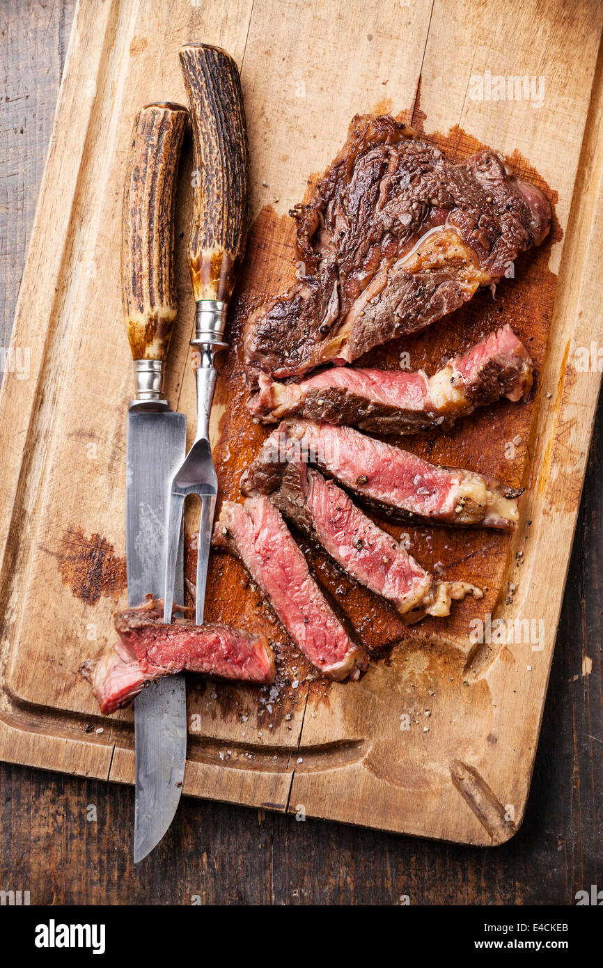 Mezzo raro grigliate di carne di manzo bistecca con coltello e forchetta per la carne sul tagliere in legno scuro dello sfondo Foto Stock