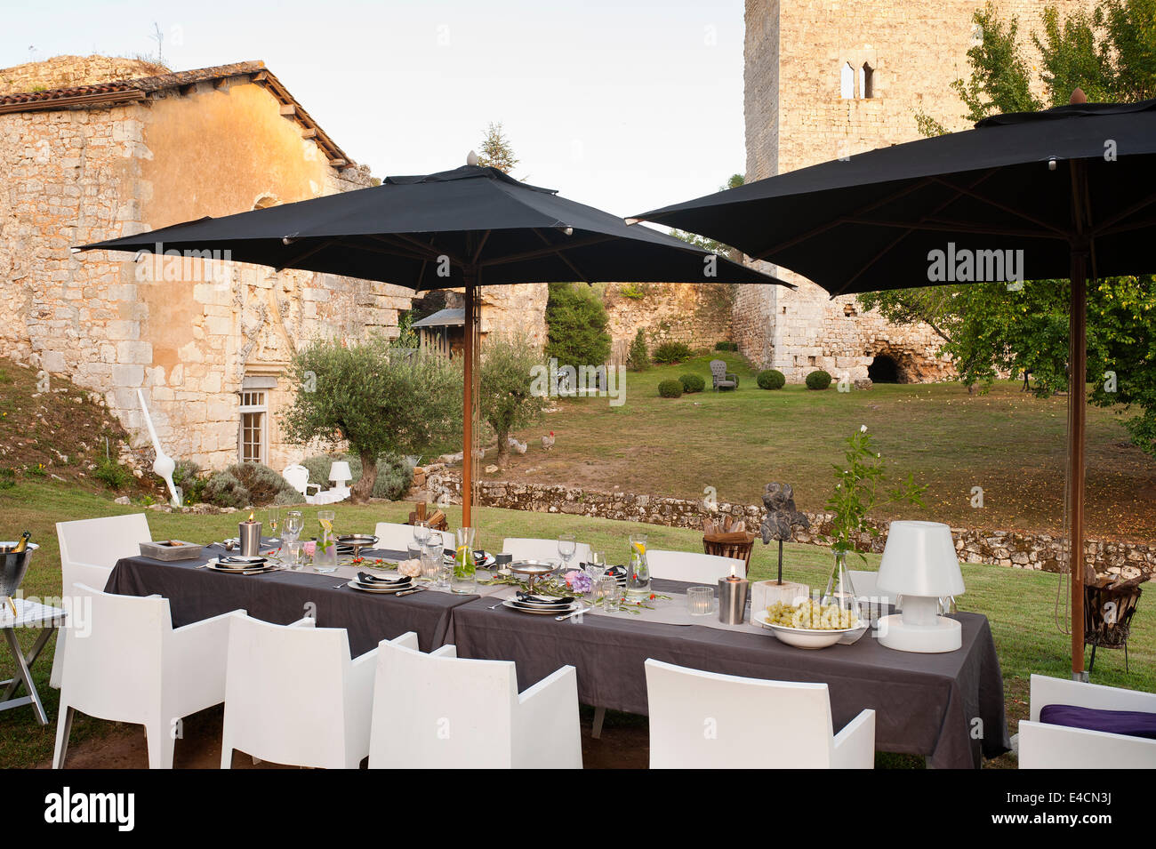Un tavolo per la cena al di sotto di una coppia di nero ombrelloni con xi secolo rovine e olivi in background. Le sedie da pranzo Foto Stock