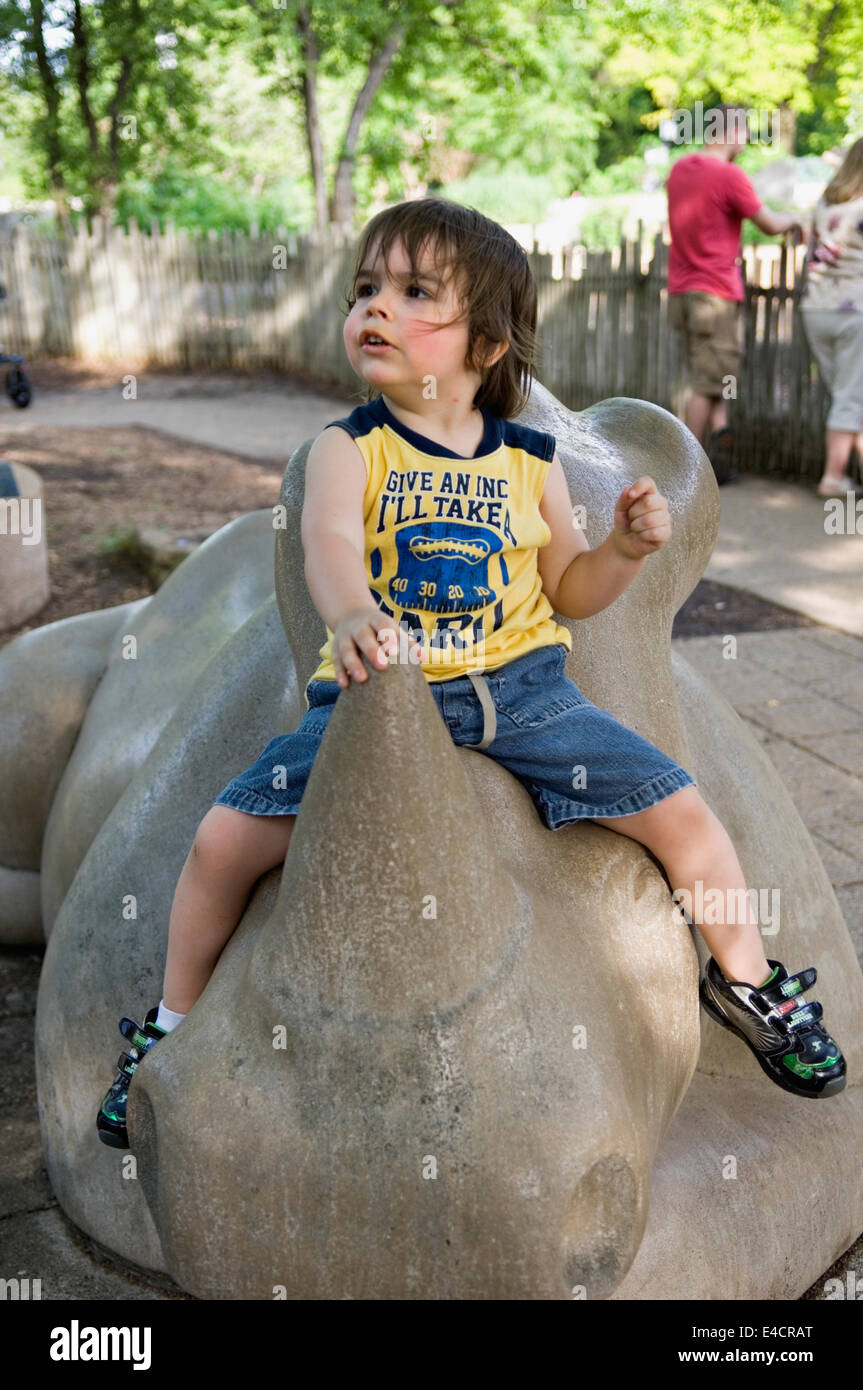 Tre anni di vecchio ragazzo seduto sul rinoceronte di scultura a lo Zoo di Louisville in Kentucky Foto Stock