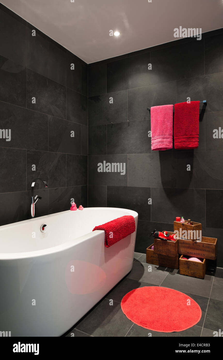 Rosso brillante e asciugamani rosa nel bagno con piastrelle di ardesia e Catalano vasca da bagno Foto Stock