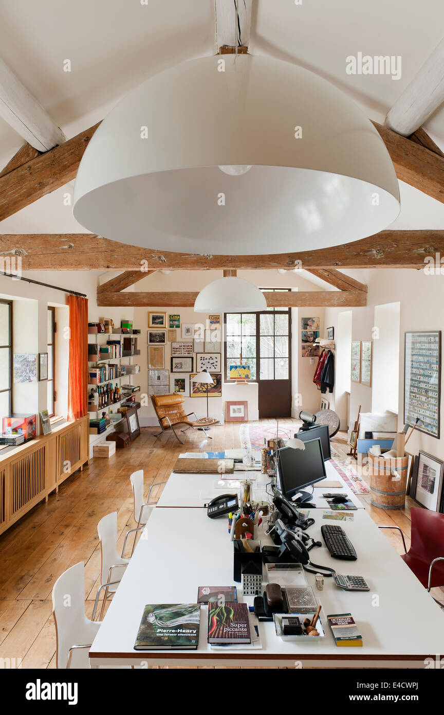 Un piano aperto uno spazio ufficio con soffitto con travi a vista, Vico Magistretti luci e FK87 Grasshopper sedia Foto Stock
