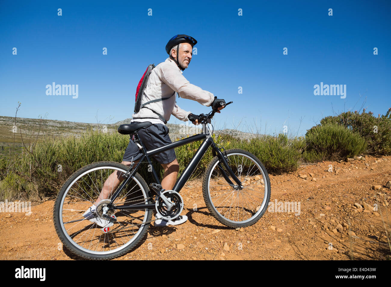 Montare il ciclista spingendo in salita in bicicletta sul terreno del paese Foto Stock