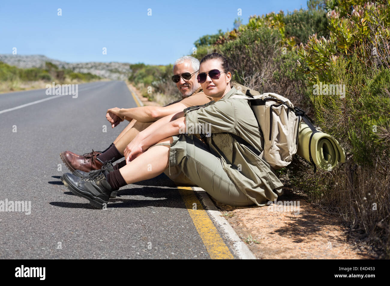 Escursionismo coppia seduta sul lato della strada sorridente in telecamera Foto Stock