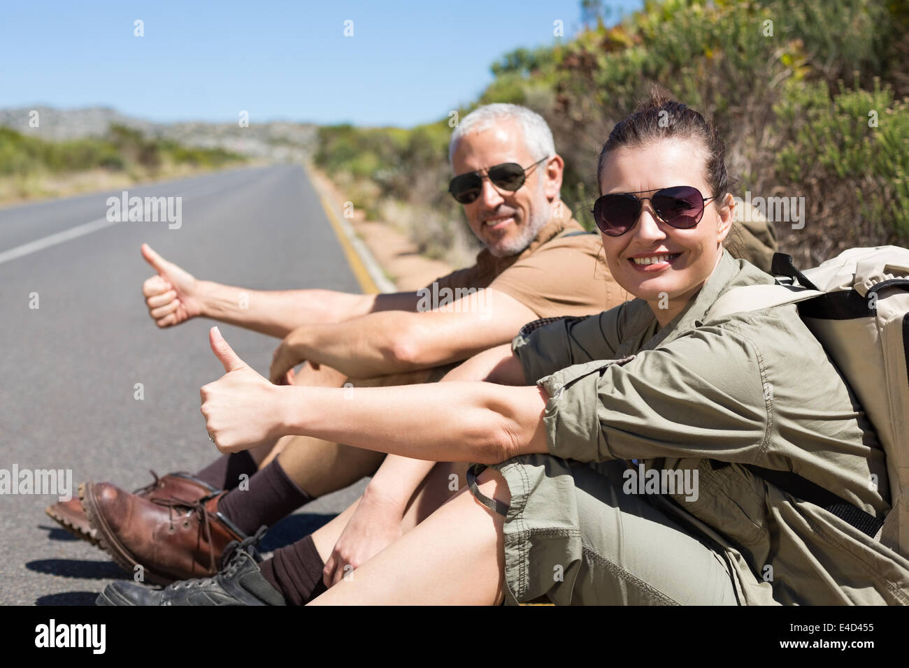 Il sollevatore escursionismo coppia seduta sul lato della strada sorridente in telecamera Foto Stock