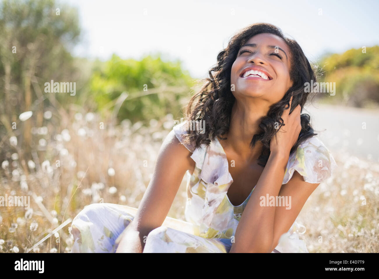 Felice bella donna seduta sul prato di abito floreale Foto Stock