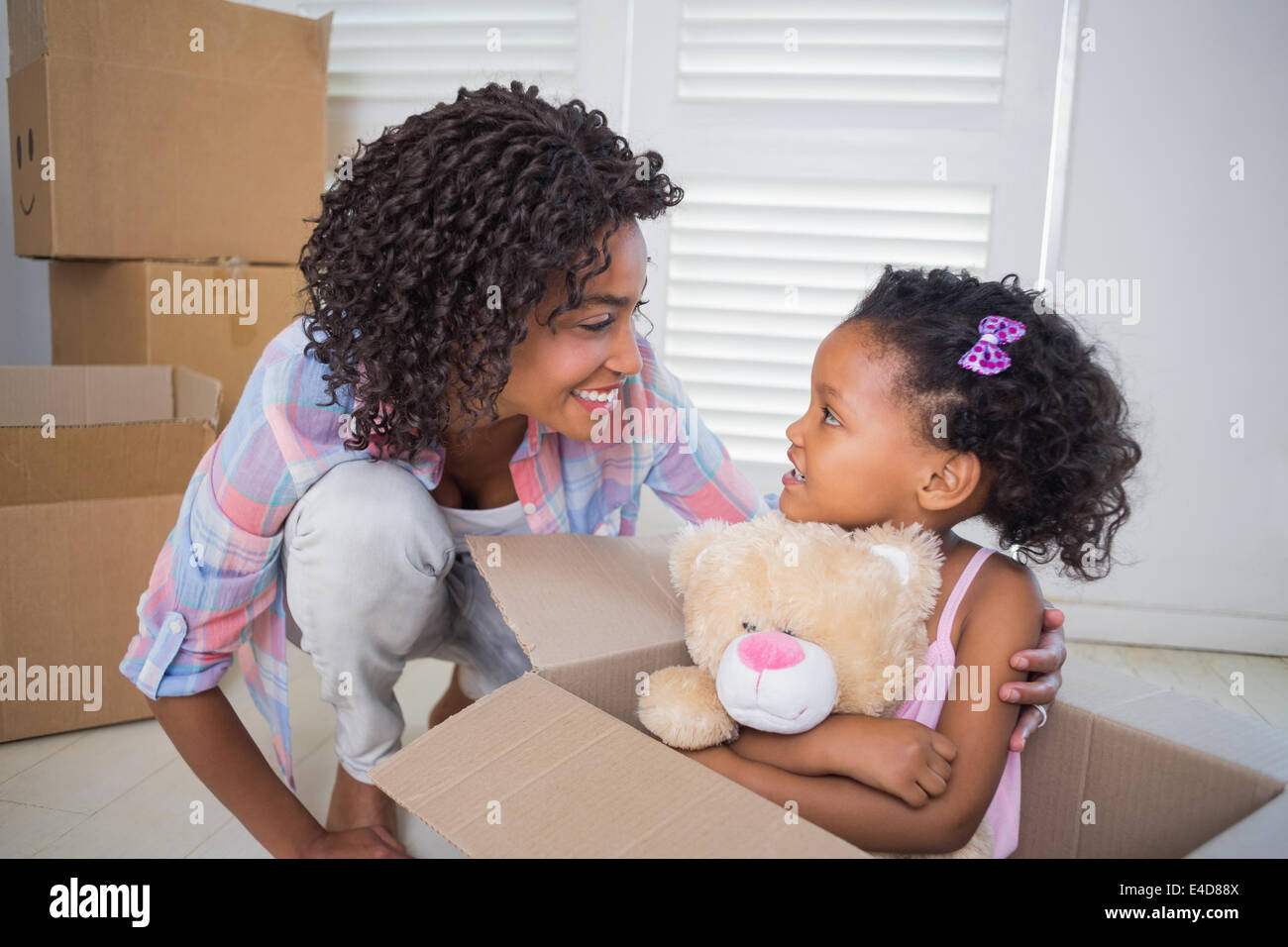 Carino figlia seduta nella scatola di movimentazione holding teddy con la madre Foto Stock