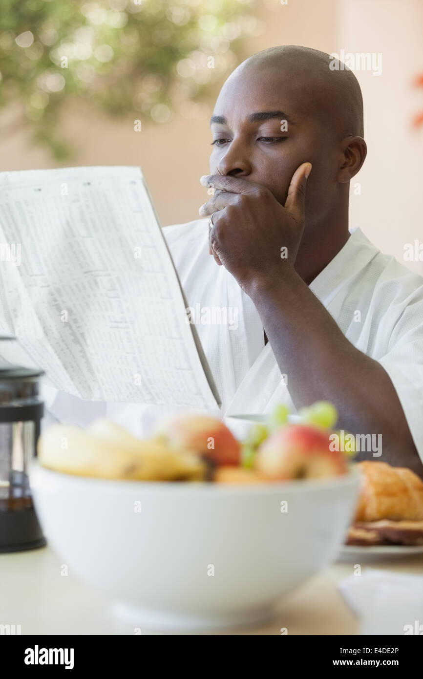 Uomo in accappatoio la lettura della carta e consumare la prima colazione sulla terrazza Foto Stock