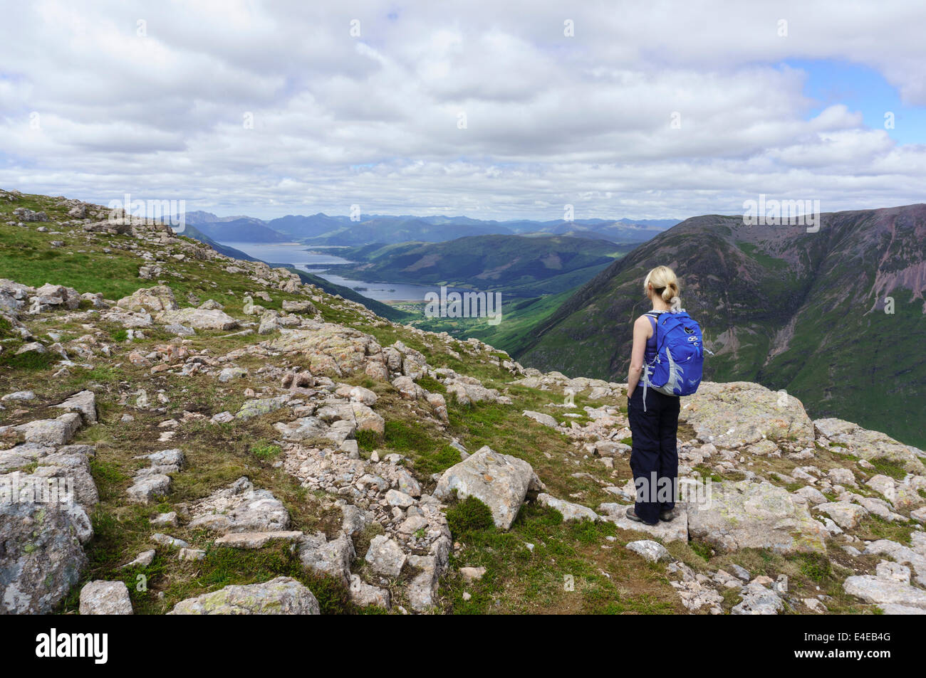 Il camminatore femmina guardando le montagne e Glencoe villaggio dalle piste di Stob Coire nan Lochan, Highlands scozzesi, Scozia, Regno Unito, Foto Stock