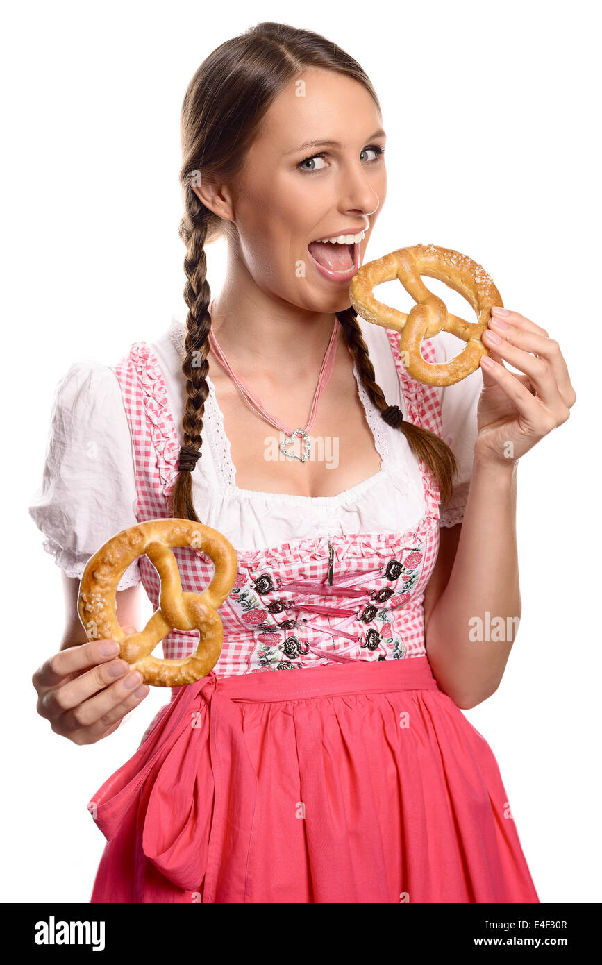Felice attraente tedesco o donna bavarese in una tradizionale dirndl aprendo la bocca per mangiare un fresco pretzel Foto Stock