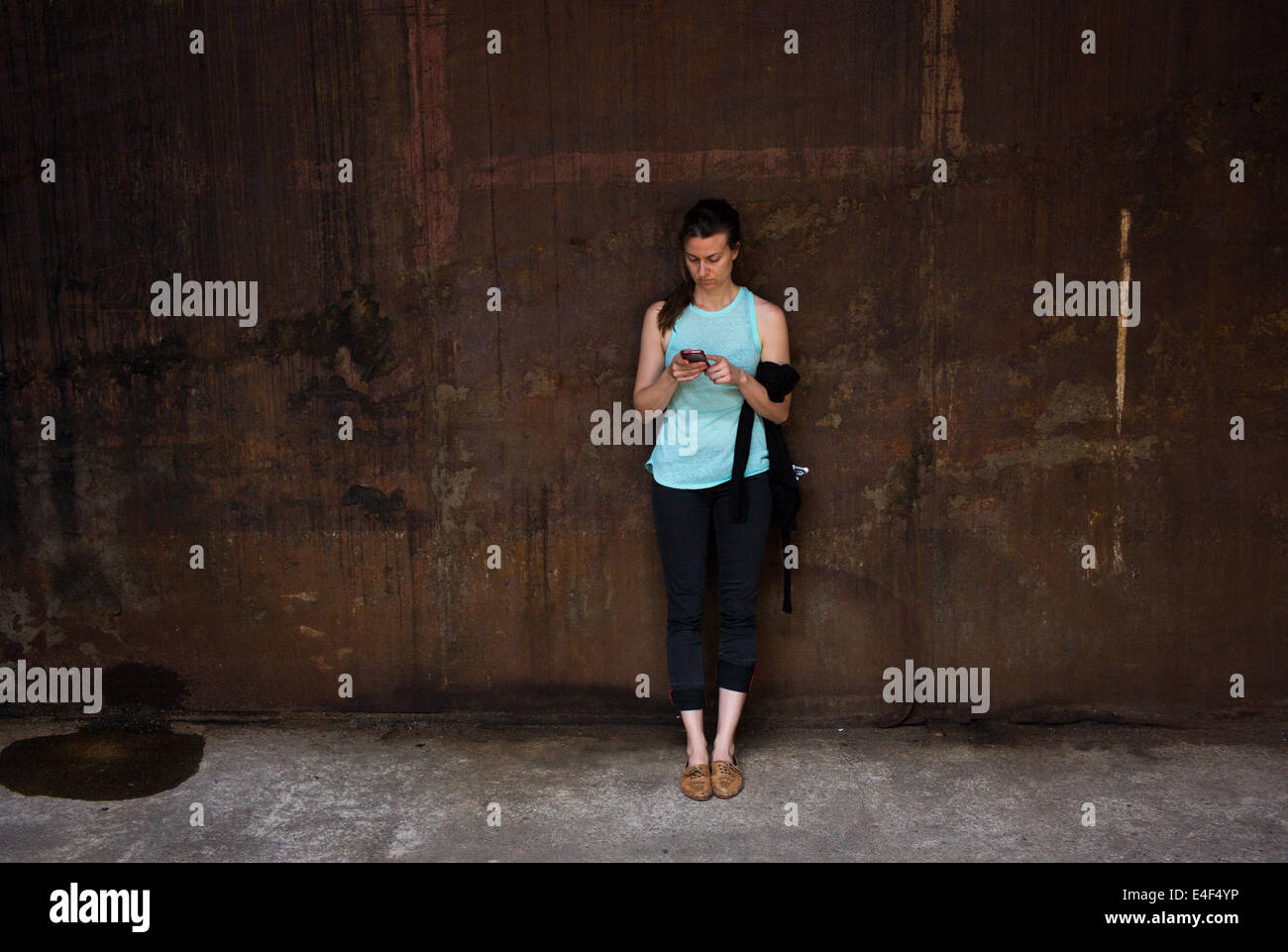 Una donna si appoggia contro una parete con il suo smart phone al Domino raffineria di zucchero a Williamsburg, New York. Foto Stock