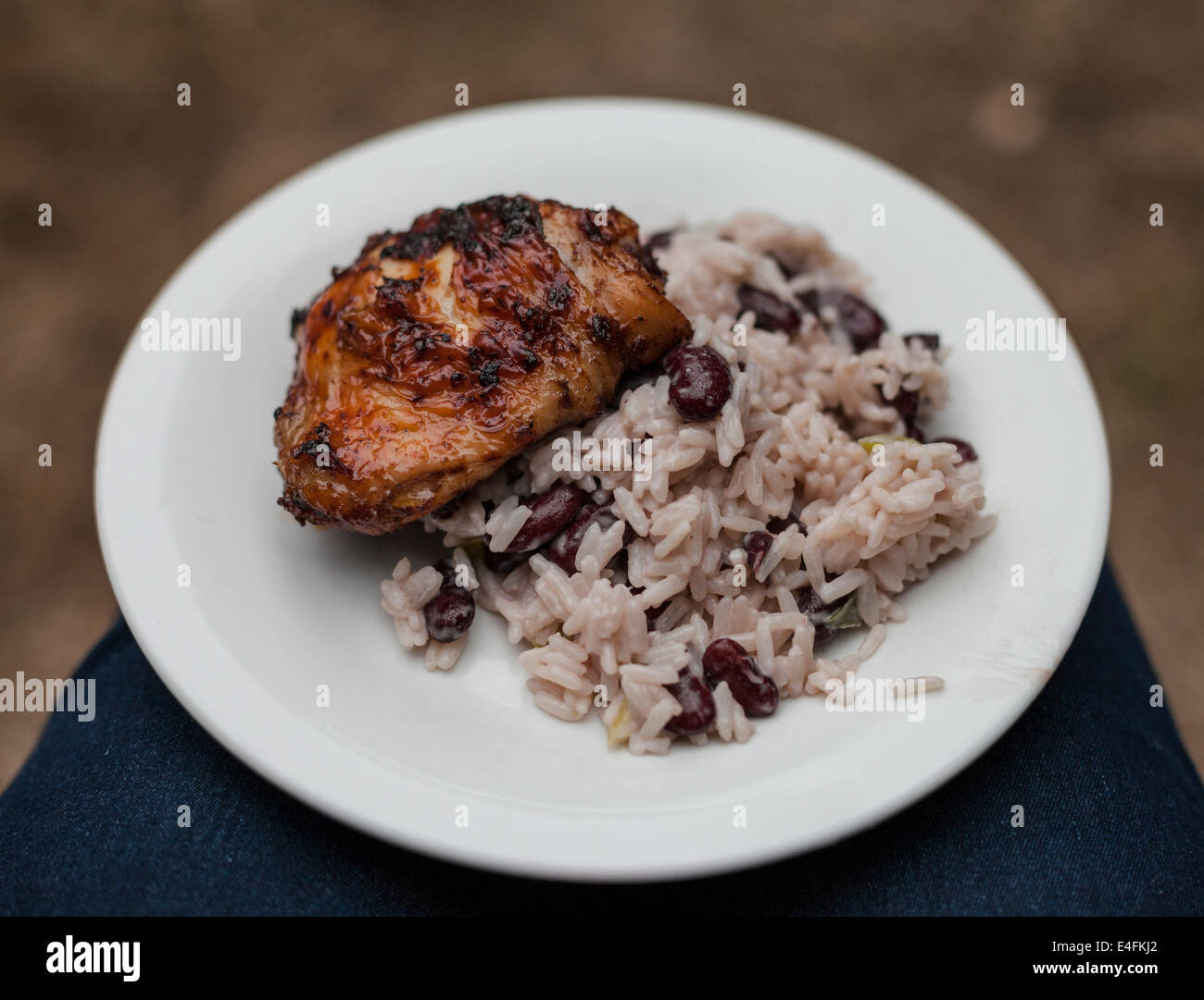 Una piastra di jerk coscia di pollo con riso e piselli bilanciato sulle ginocchia a un barbecue estivo. Foto Stock