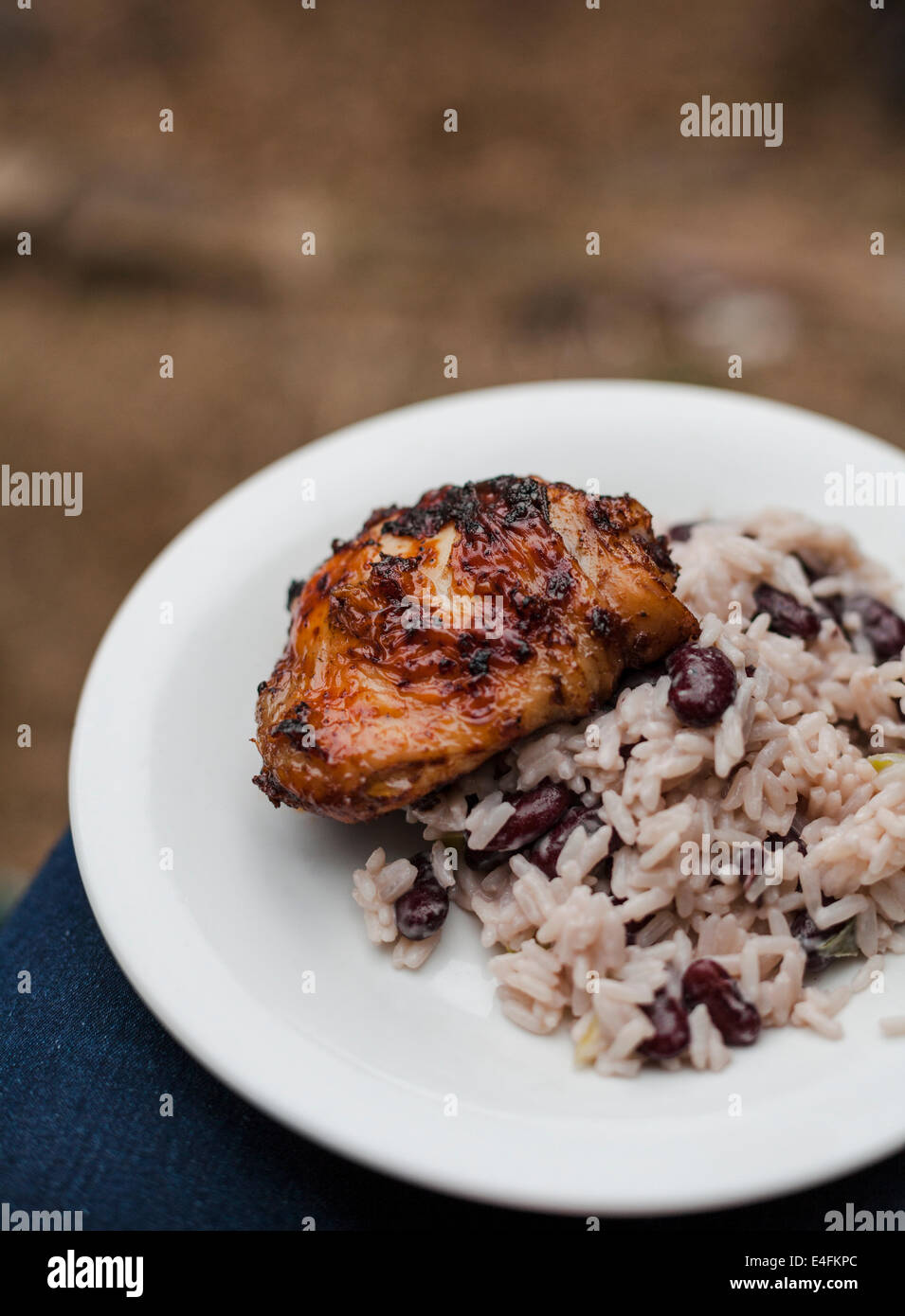 Una piastra di jerk coscia di pollo con riso e piselli bilanciato sulle ginocchia a un barbecue estivo. Foto Stock