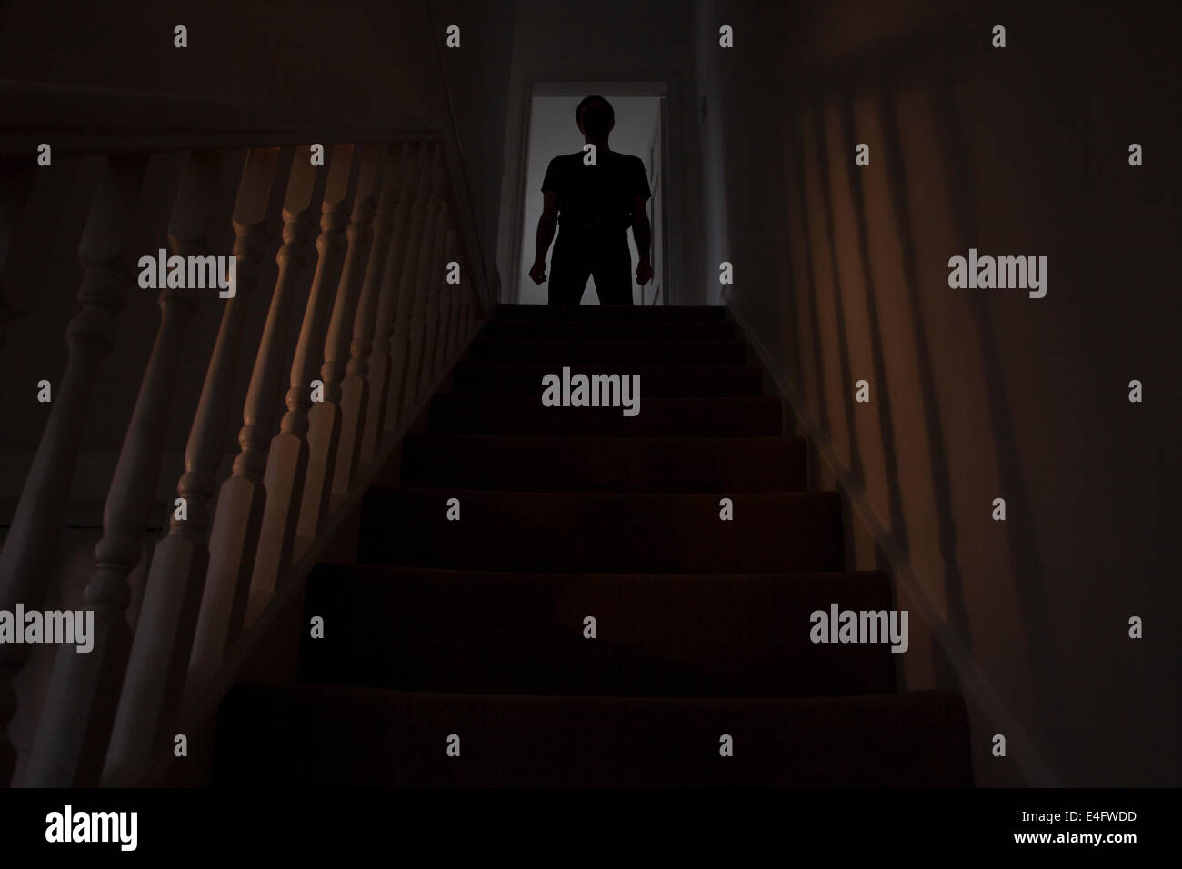 Silhouette di un uomo in piedi alla cima di una scalinata, ombre sulle pareti dalla luce di seguito. Vedere immagini simili. Foto Stock