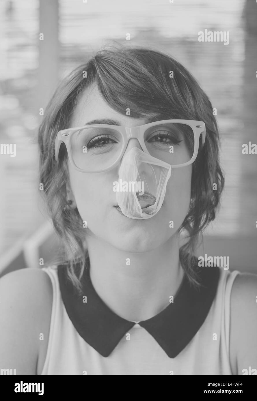 Carino hipster ragazza adolescente con grandi gomme da masticare bubble popping oltre il suo volto. In bianco e nero in stile retrò immagini Foto Stock