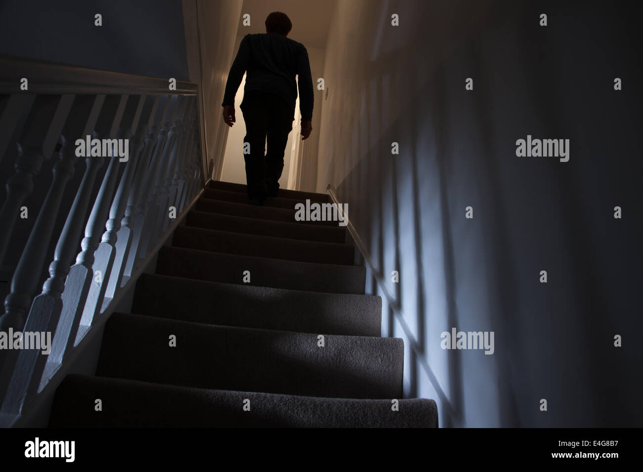 Silhouette di un uomo a camminare al piano superiore vista posteriore, le ombre proiettate sulle pareti dalla luce di seguito. Foto Stock