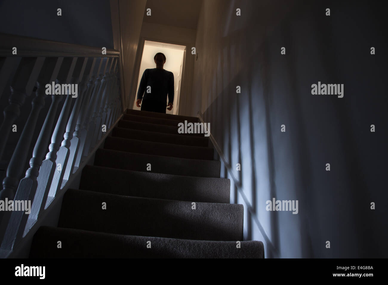 Silhouette di un uomo in piedi alla cima di una scalinata, ombre sulle pareti dalla luce di seguito. Foto Stock