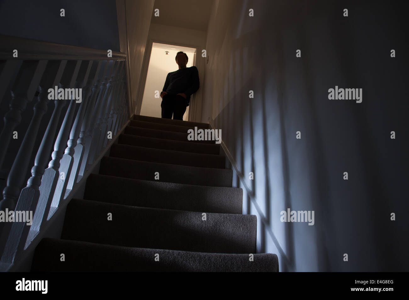 Silhouette di un uomo appoggiata contro il muro alla sommità di una scalinata, ombre sulle pareti dalla luce di seguito. Foto Stock