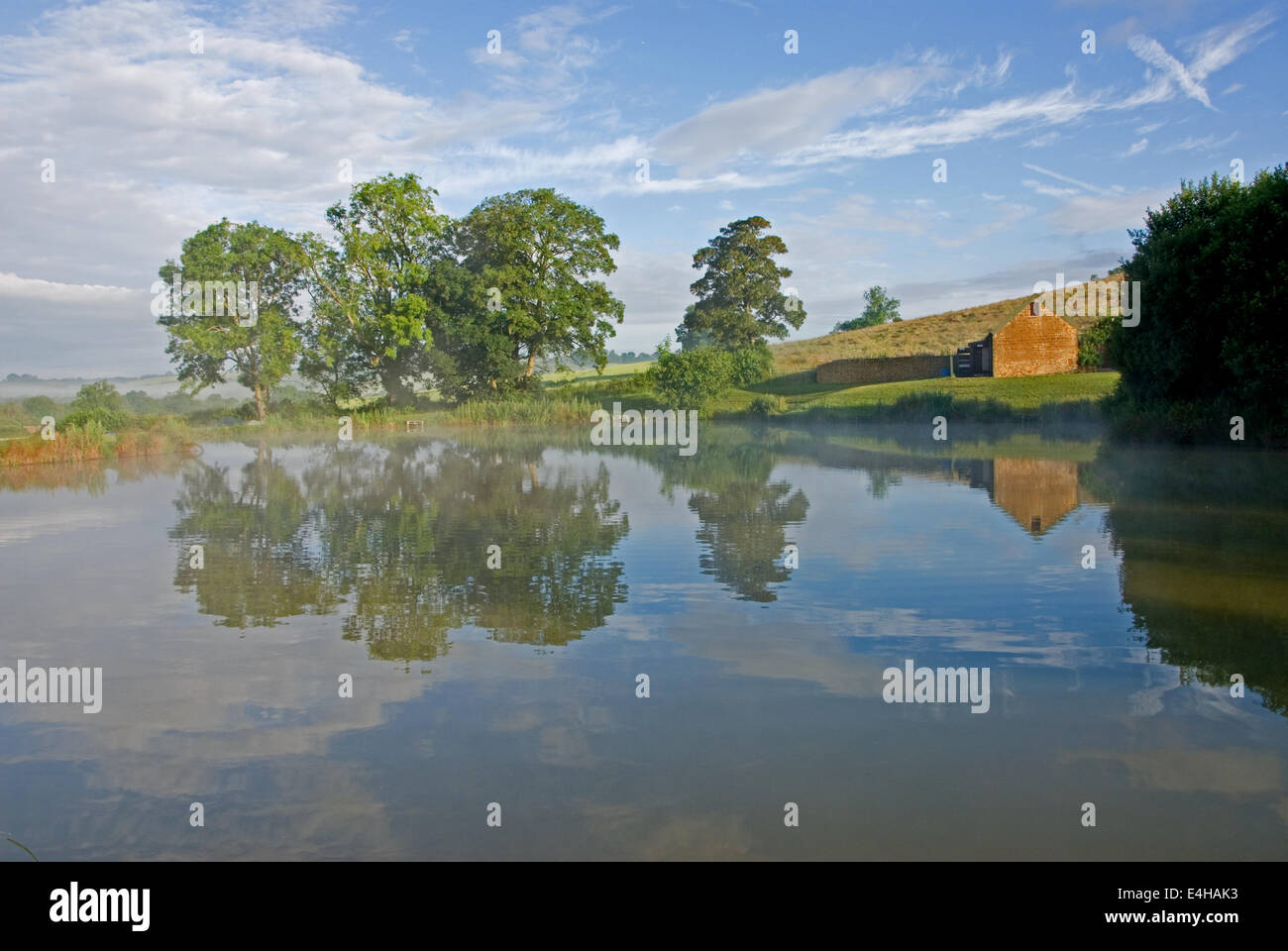 Gli alberi si riflette ancora in acqua di un lago, con nebbia di salita . Foto Stock