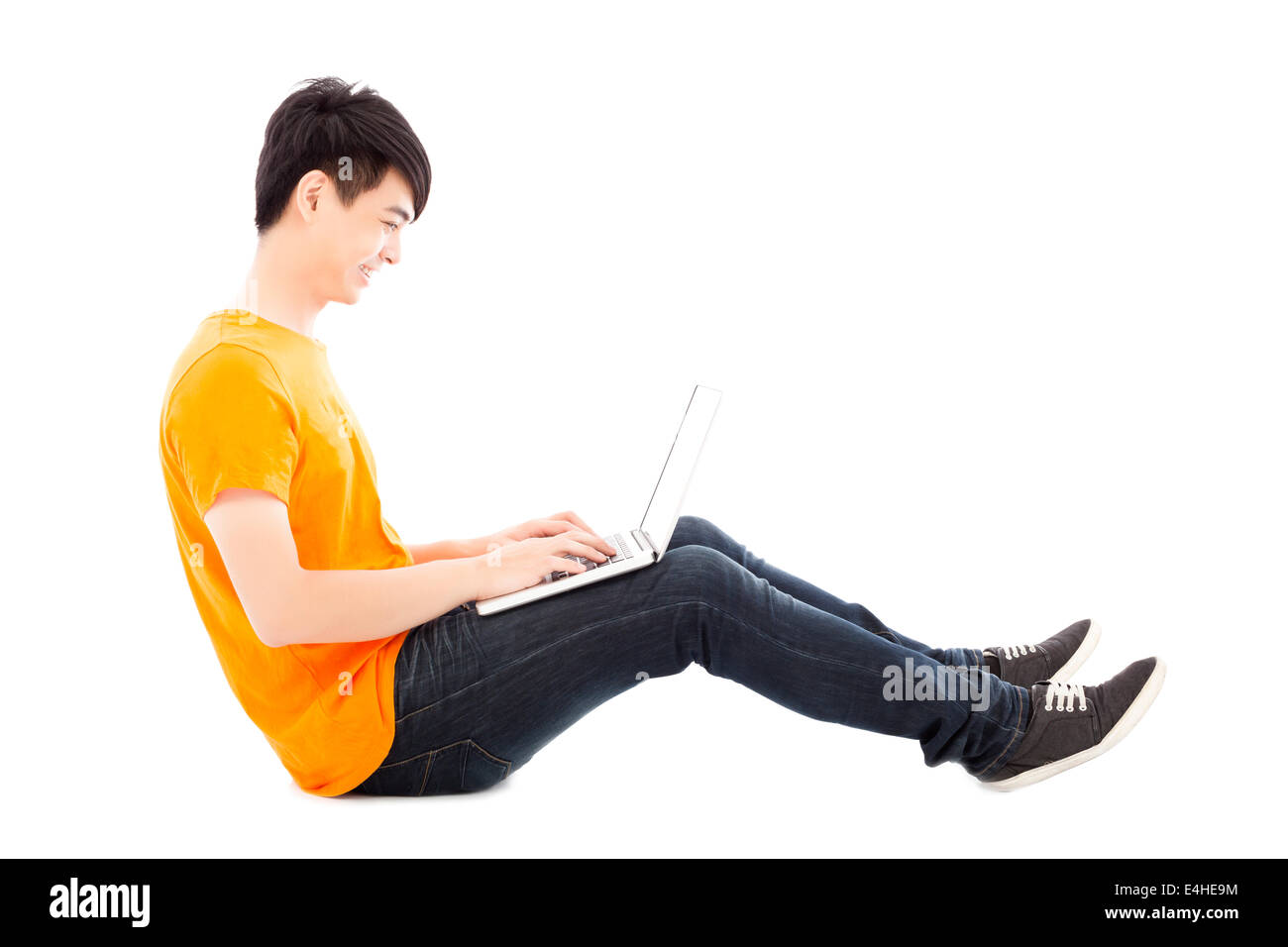 Felice giovane studente seduto sul pavimento e utilizzando computer portatile Foto Stock
