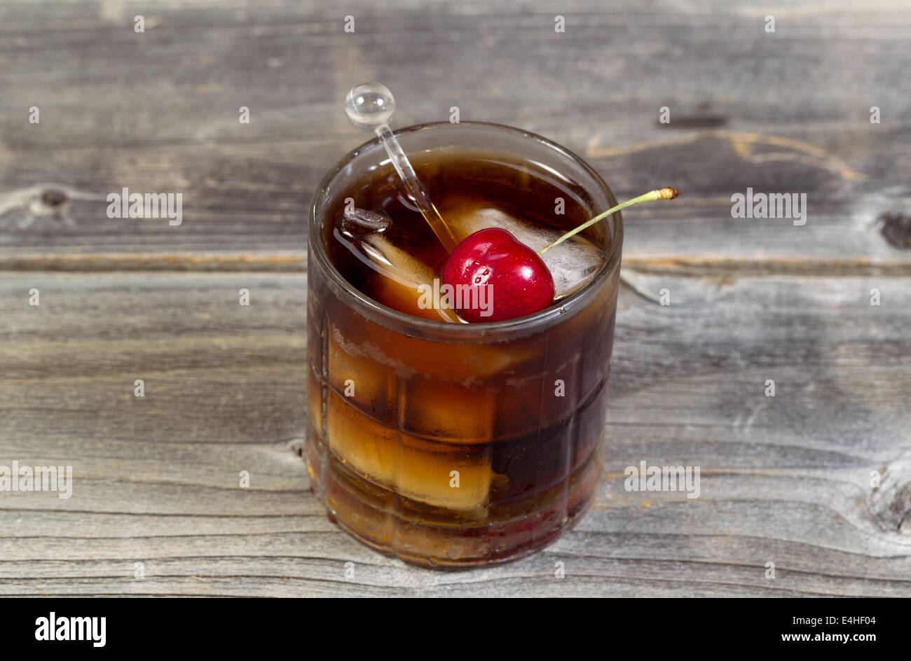 Parte superiore orizzontale vista di un rum e cola con grande ciliegia di colore rosso e il ghiaccio in vetro in posizione sul legno rustico Foto Stock