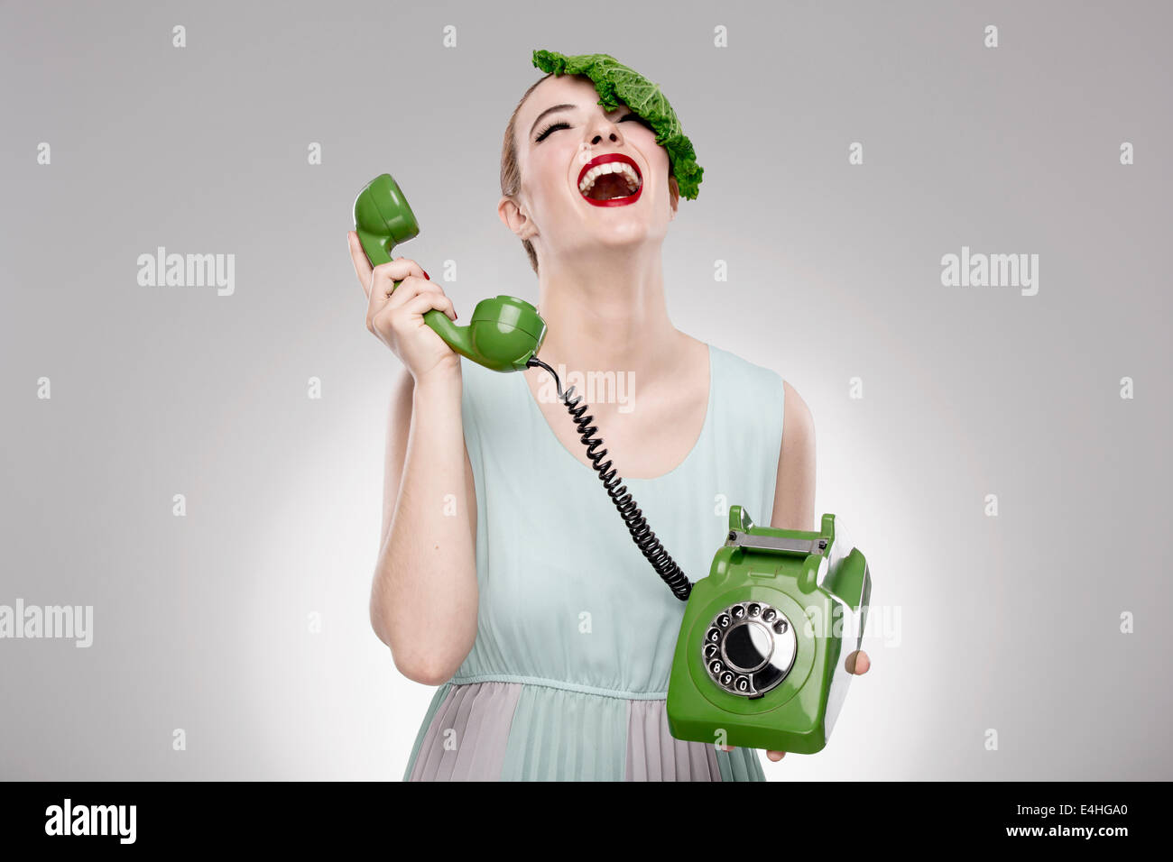 Ritratto di una donna che illustra un concetto vegano con un cavolo cappuccio sulla testa e facendo un ecologico chiamata verde Foto Stock