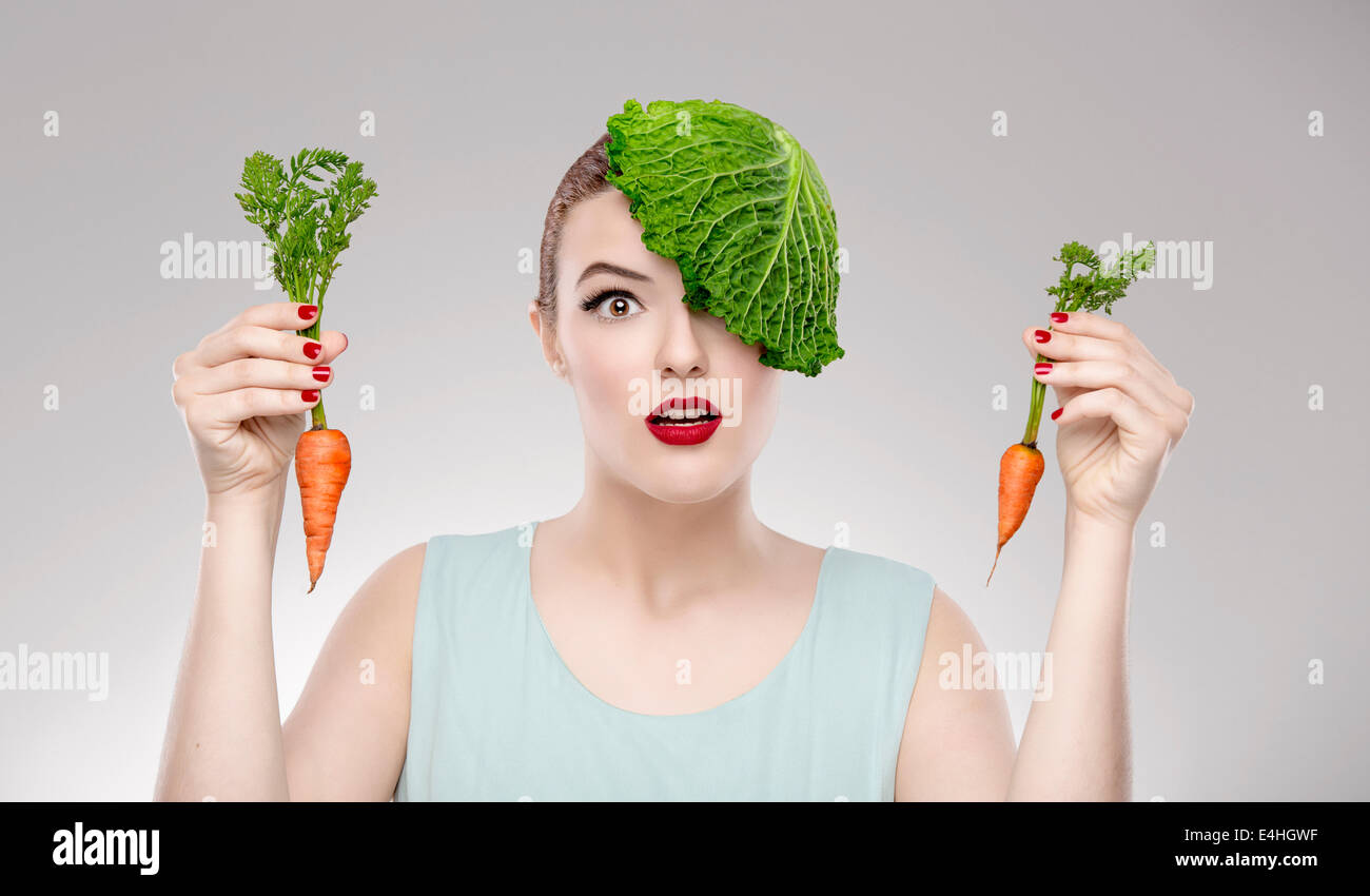 Ritratto di una donna che illustra un concetto vegano tenendo un carote e con un cavolo cappuccio sulla testa Foto Stock