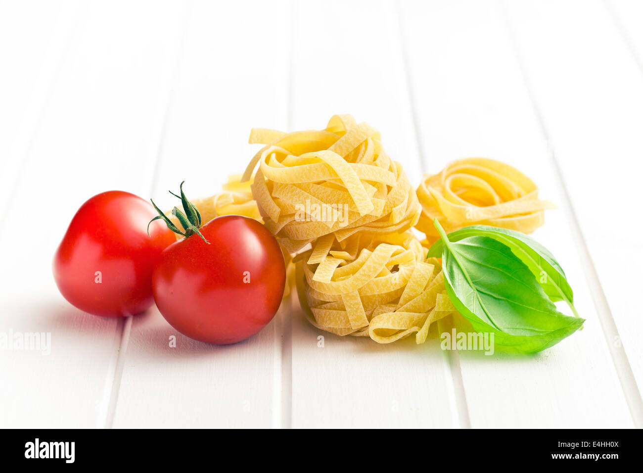 La pasta italiana Le tagliatelle, i pomodori e le foglie di basilico sul tavolo bianco Foto Stock