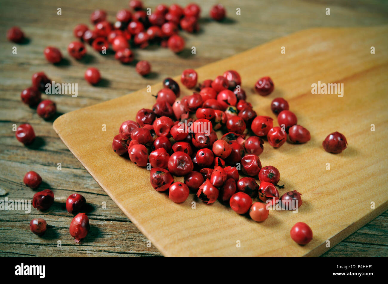 Un mucchio di grani di pepe rosa su una tavola in legno rustico Foto Stock