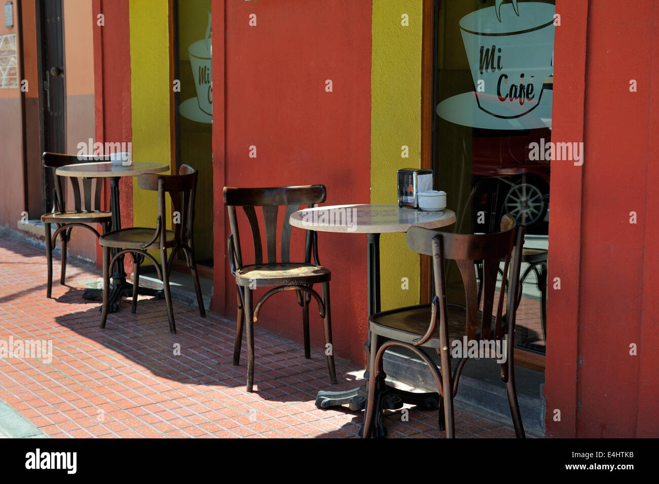 Svuotare cafe con tavolo e sedie da esterno contro il rosso e il giallo muro Foto Stock