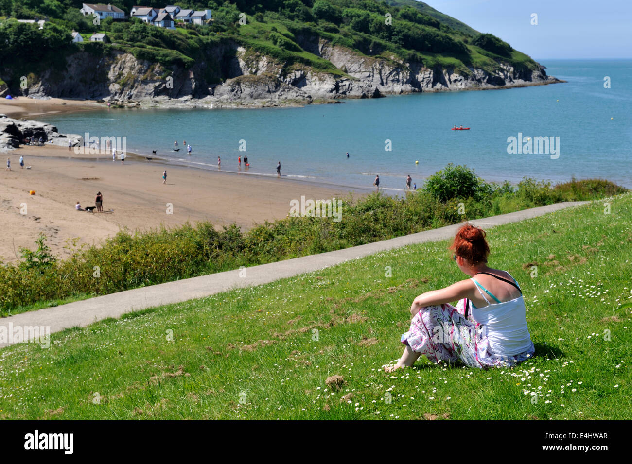 Giovane donna seduta nel parco guardando verso il basso sulla spiaggia di Aberporth Cardigan Bay, Pembrokeshire, West Wales, Regno Unito Foto Stock