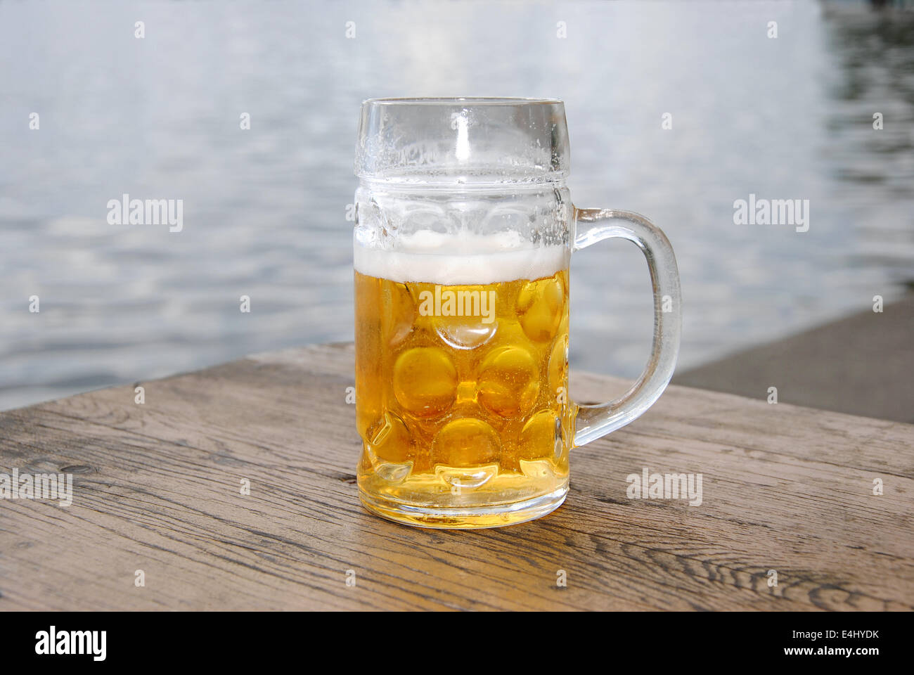 Boccale di birra con birra fresca e schiuma su una tavola di legno in un giardino della birra sul lago, vicino fino Foto Stock