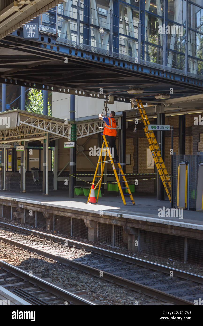 Questa immagine mostra un ingegnere elettrico lavorando sul cablaggio sulla parte inferiore di una passerella a una Ferrovia Nazionale stazione ferroviaria Foto Stock