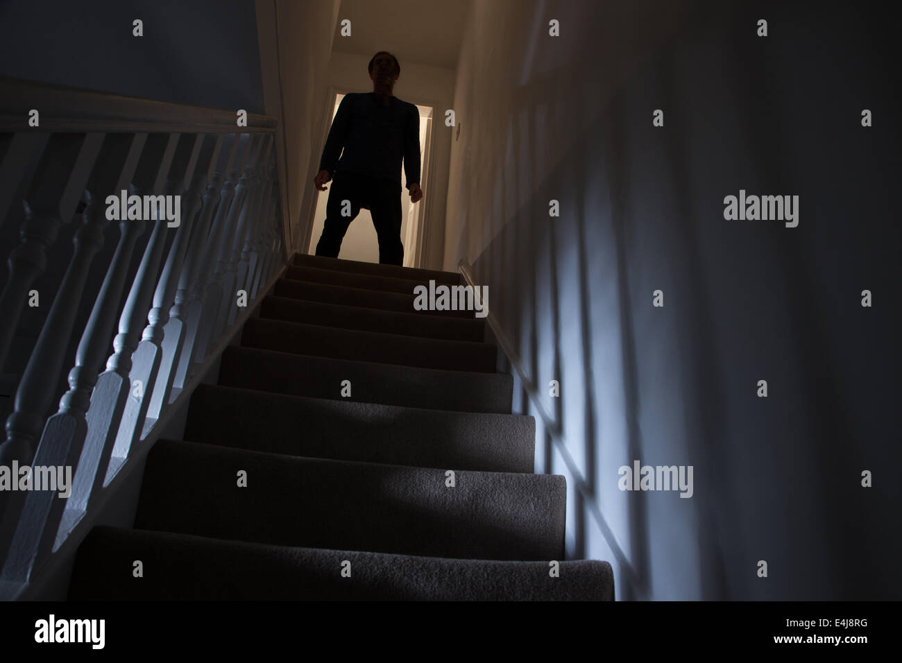 Silhouette di un uomo in piedi alla cima di una scalinata, ombre sulle pareti dalla luce di seguito. Foto Stock