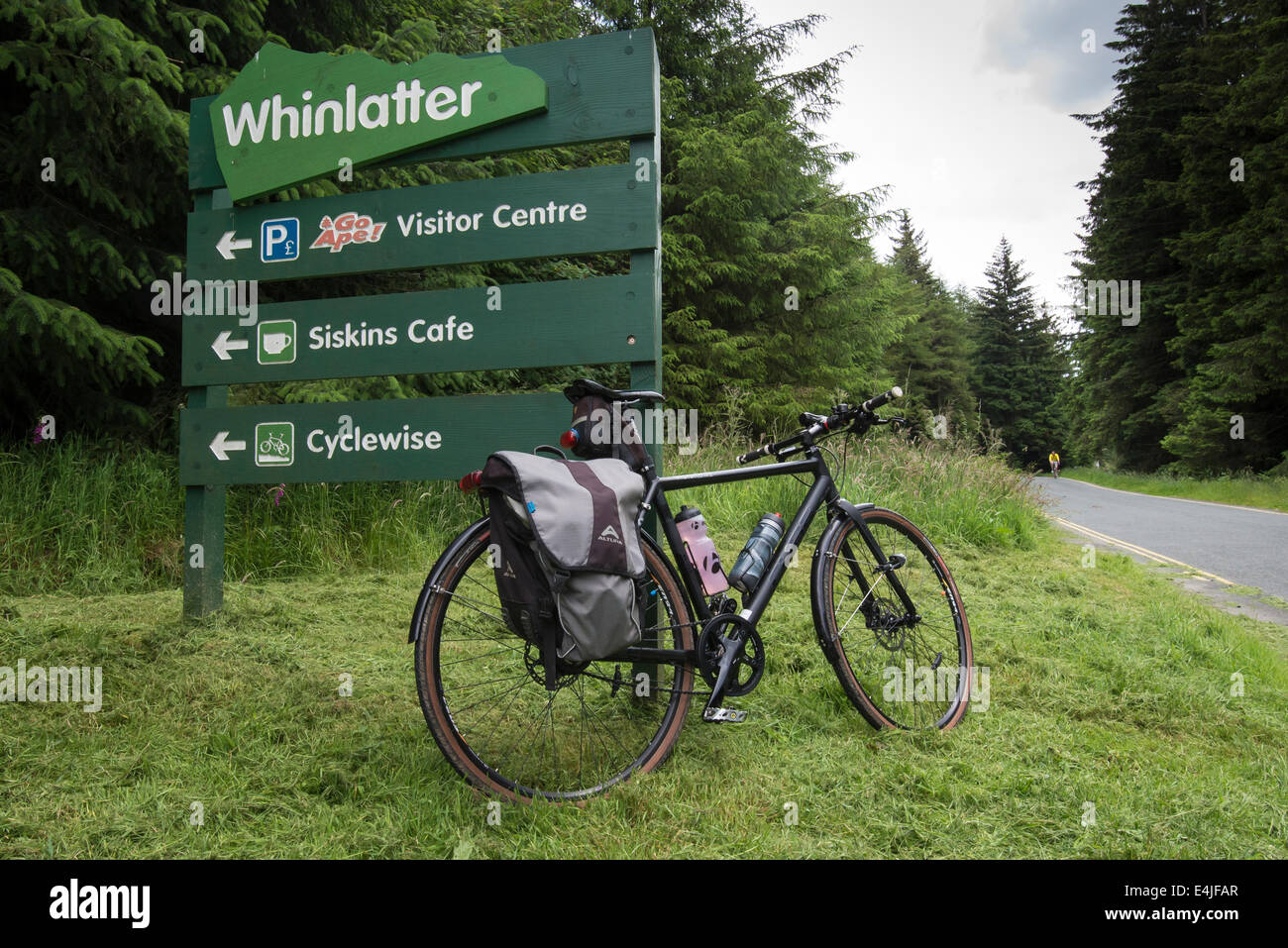 Un cubo Hooper hybrid bike in cima Whinlatter passano in appoggio contro il cartello vicino alla strada Foto Stock