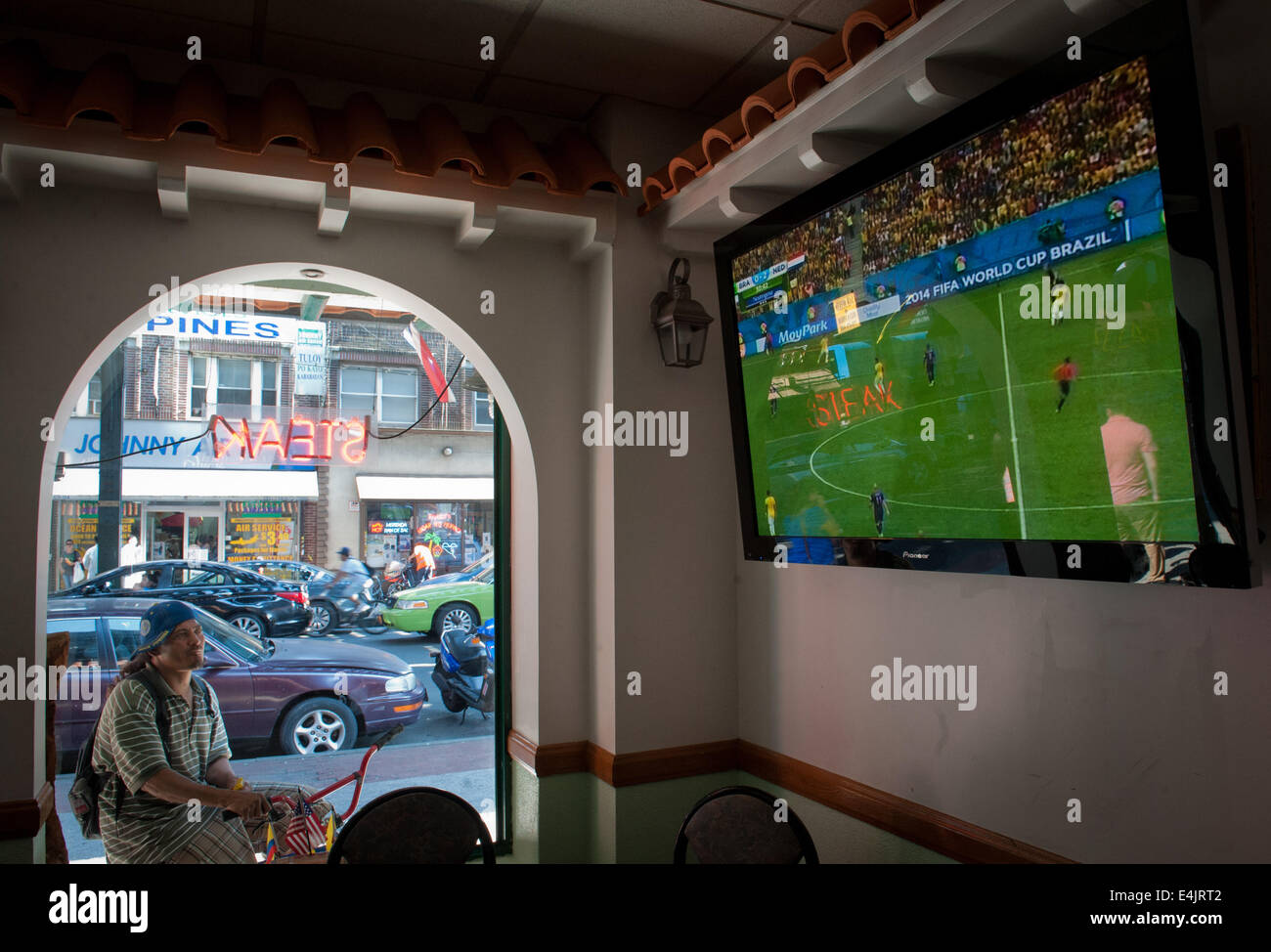 Queens, a New York, Stati Uniti d'America. 12 Luglio, 2014. Un uomo su una bicicletta consente di mettere in pausa per catturare il cliente come il ristorante Pollos ala Brasa Marion a Roosevelt Avenue televises la corrispondenza tra il Brasile e i Paesi Bassi per il terzo posto nella Coppa del Mondo 2014 su Univision, Sabato, 12 luglio 2014. © Bryan Smith/ZUMA filo/Alamy Live News Foto Stock