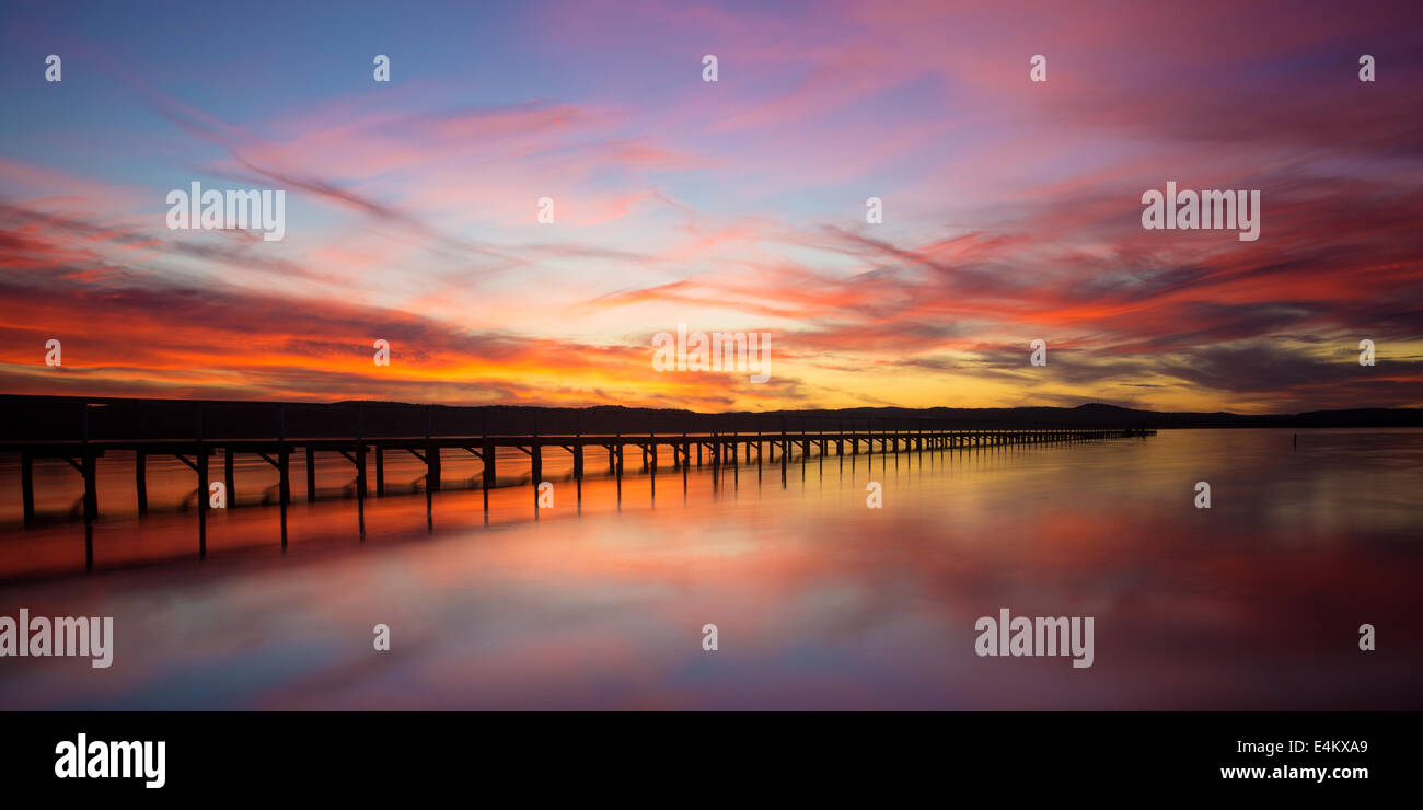 Lungo molo in NSW, Australia al tramonto con il cielo rosso che viene riflessa nell'acqua Foto Stock