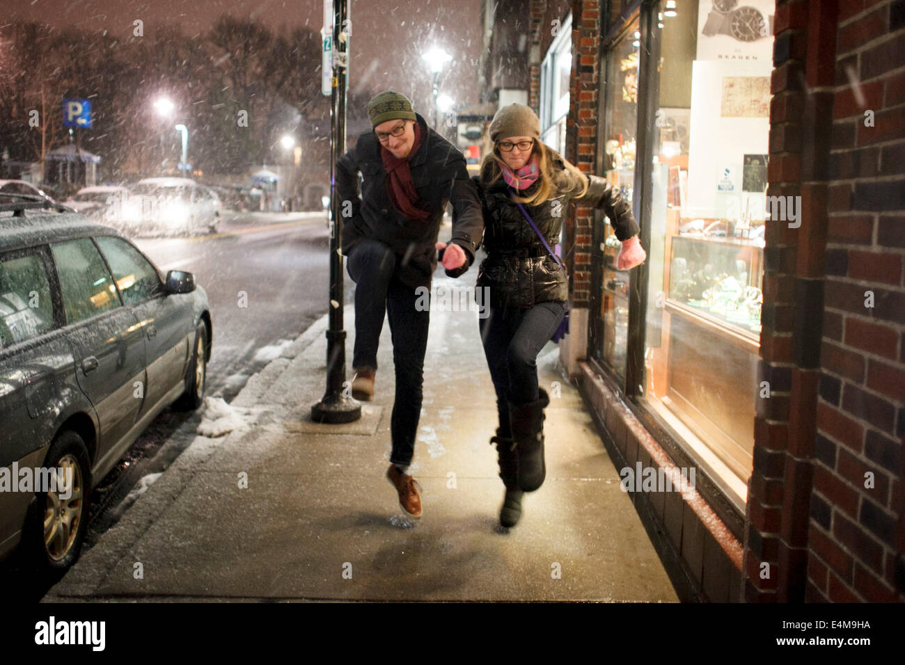 Giovane saltando in neve sul marciapiede urbano di notte Foto Stock