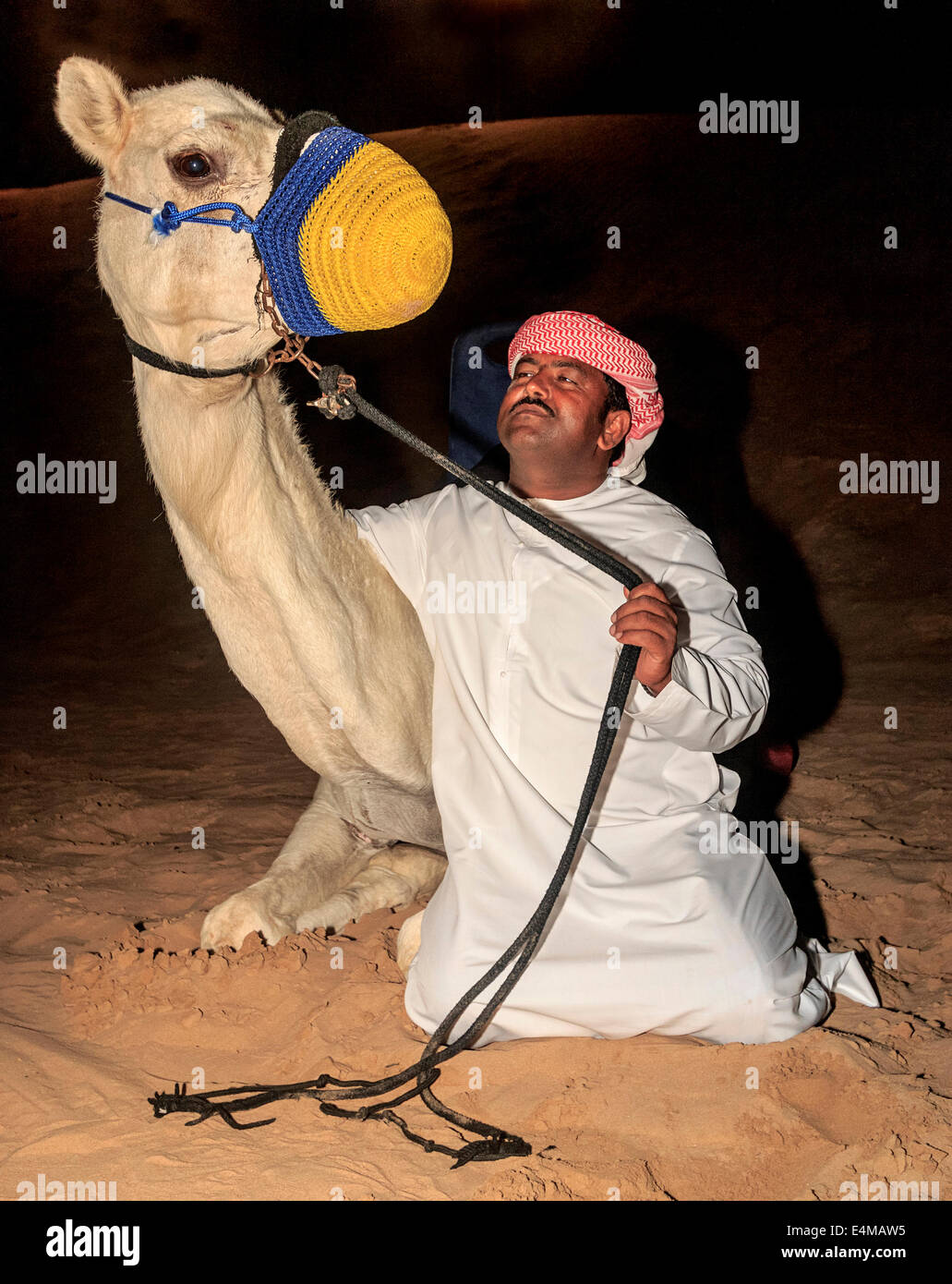 Uomo beduino nel tradizionale abito arabo pone con il suo cammello in un safari nel deserto camp fuori Dubai, UAE, dove i visitatori possono di Foto Stock