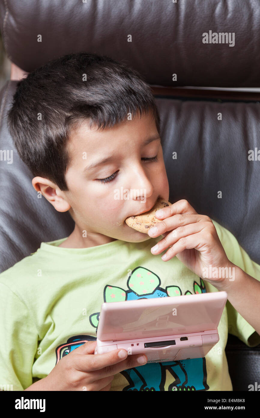 Ragazzo gioca giochi per computer e mangia biscotti Foto Stock