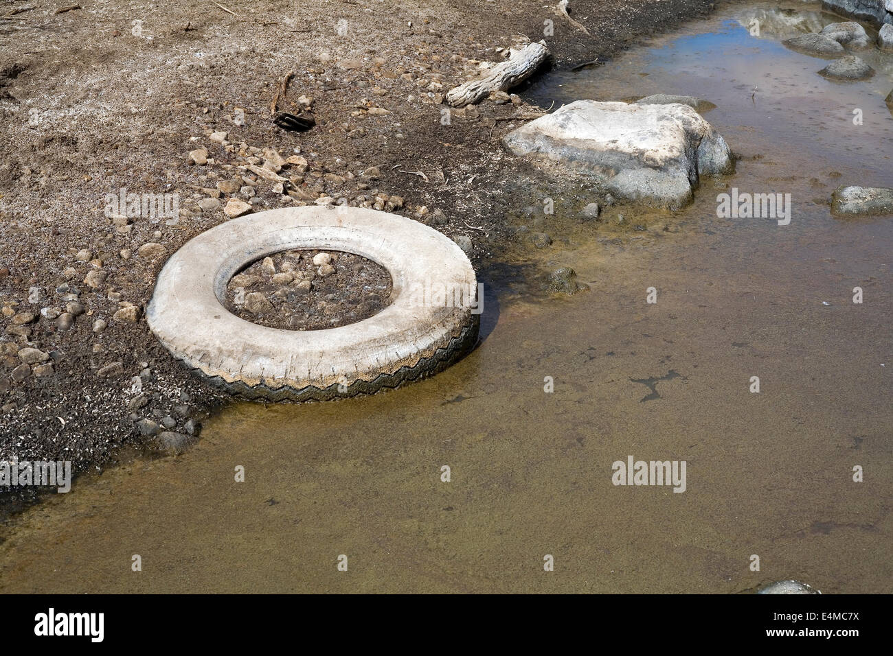 Vecchio pneumatico pneumatico oggetto di dumping in un letto del fiume. Foto Stock