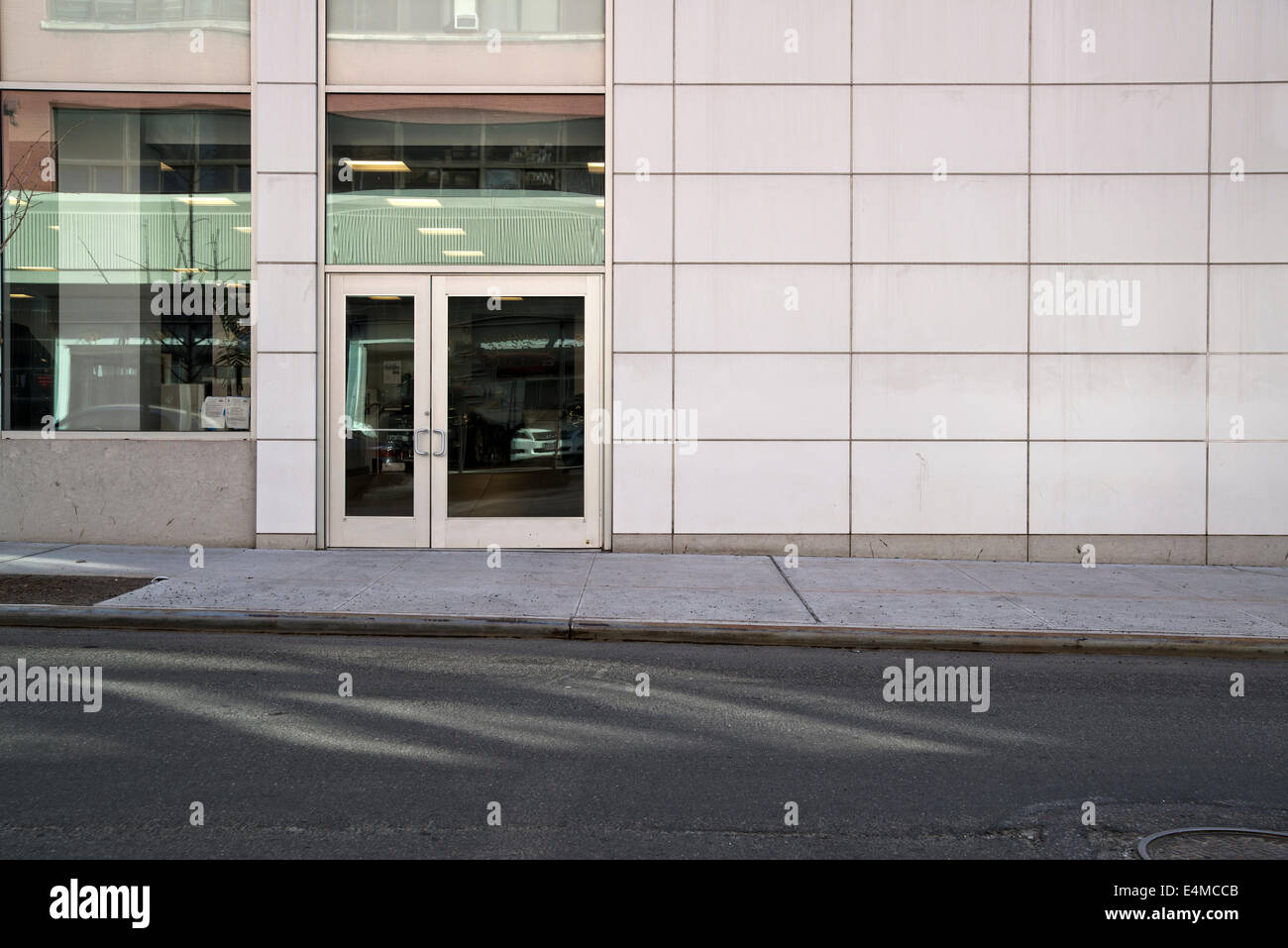 Parete piastrellata e porta di ingresso di un'Auto Showroom, il sole splende riflessioni sul marciapiede. La città di New York. Foto Stock