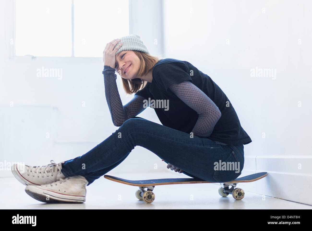 Giovane donna seduta su skateboard Foto Stock