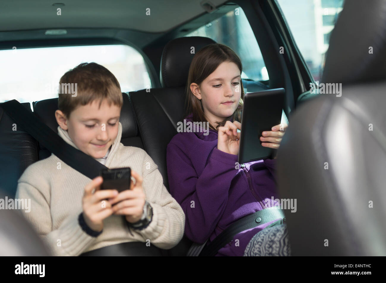 Un ragazzo e una ragazza (8-9, 10-11) utilizzando la tavoletta digitale e smart phone in auto Foto Stock