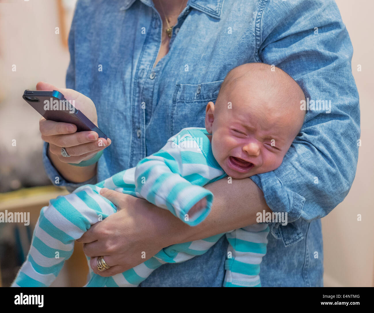 Donna sms e tenendo il pianto baby boy (2-5 mesi) Foto Stock