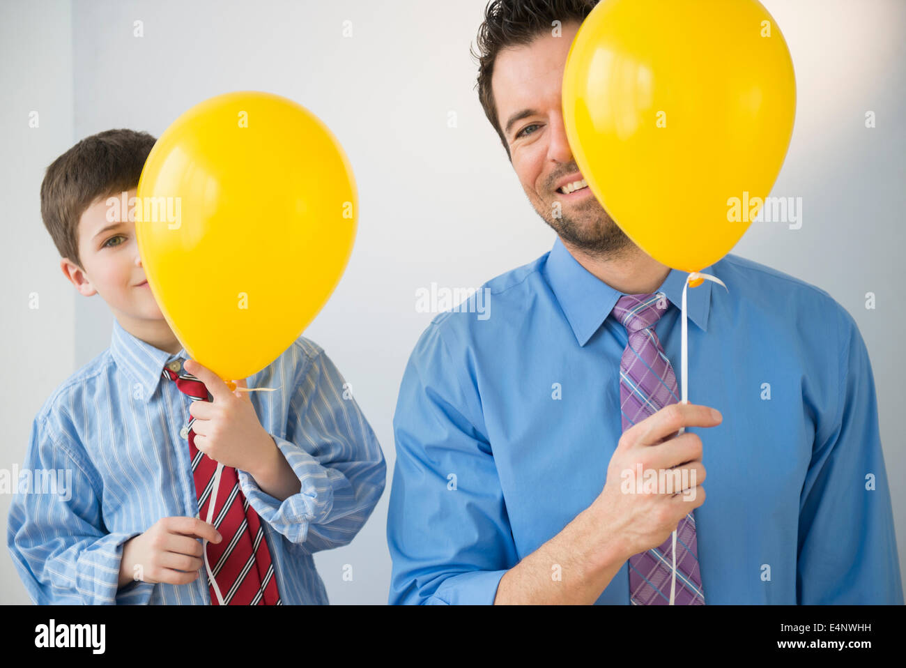 Padre e figlio (8-9) peeking dietro palloncini gialli Foto Stock